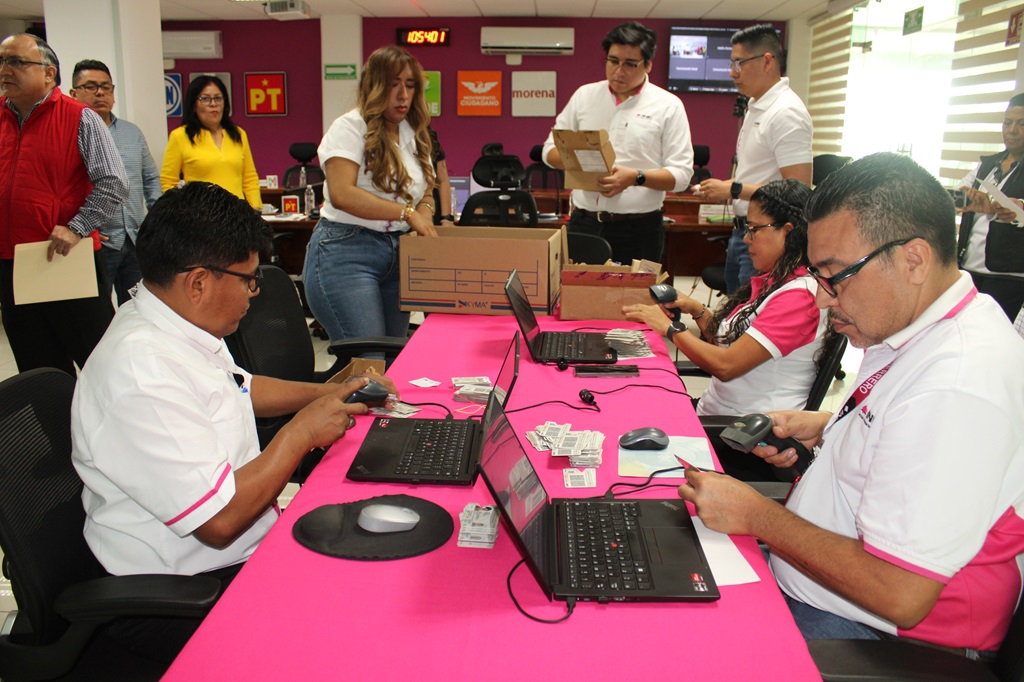 Tres personas sentadas en una mesa frente a computadoras revisando credenciales para votar