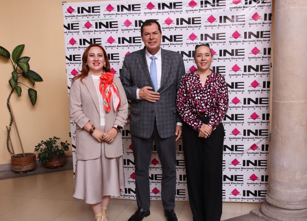 dos mujeres y un hombre de pie frente a una manta con letras negras y cuadros rosas