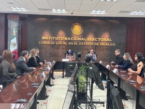 Nueve personas sentadas en una mesa alargada detrás de micrófonos.