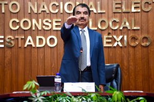 hombre de pie, cabello negro bigote y saco azul con el brazo extendido al frente