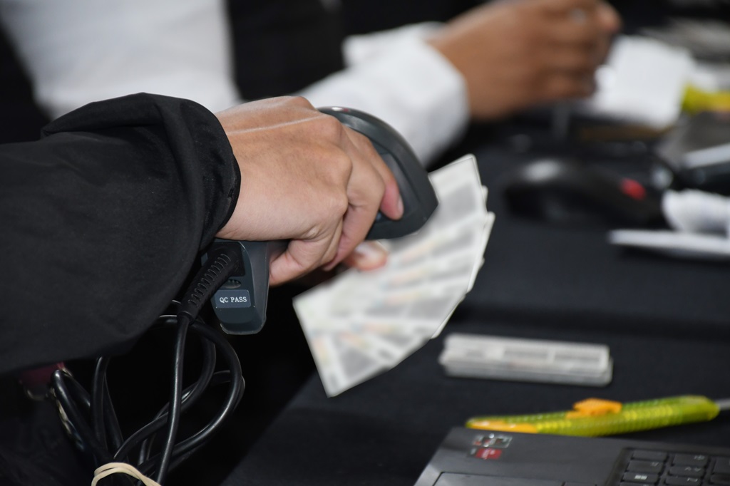 Se muestra una mano sosteniendo un verificador apuntando a credenciales para votar.