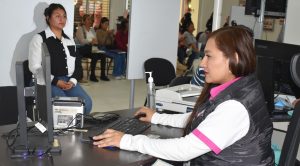 dos mujeres, una sentada mirando al frente y otra a su lado, frente a una computadora