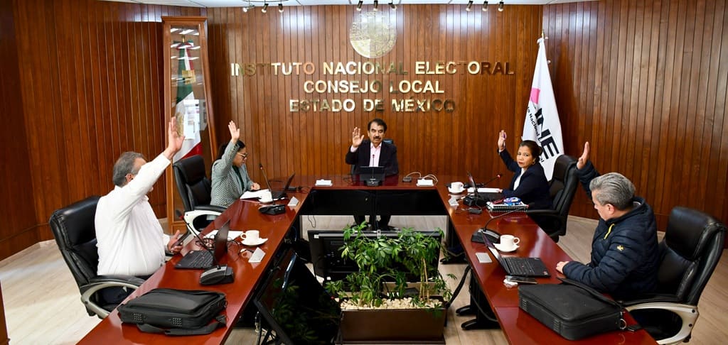 cinco personas sentadas alrededor de una mesa ovalada votando a mano alzada