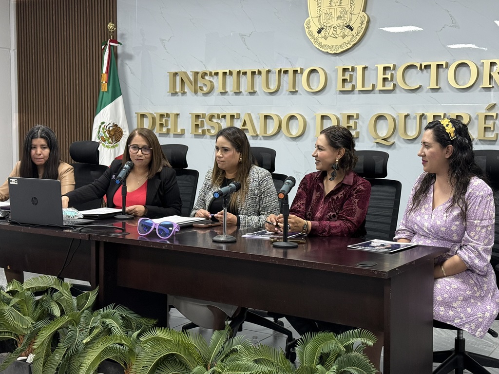 Cinco mujeres sentadas detrás de una mesa, hablando a través de micrófonos.