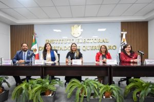 Cinco personas sentadas detrás de una mesa larga hablando detrás de micrófonos