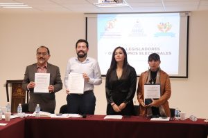 Cuatro personas de pie detrás de una mesa sosteniendo documentos