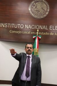 hombre de pie bigote cabello negro corto, con el brazo derecho extendido al frente