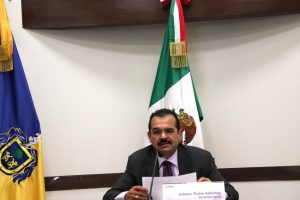 hombre sentado, bigote con lentes, leyendo frente a un micrófono