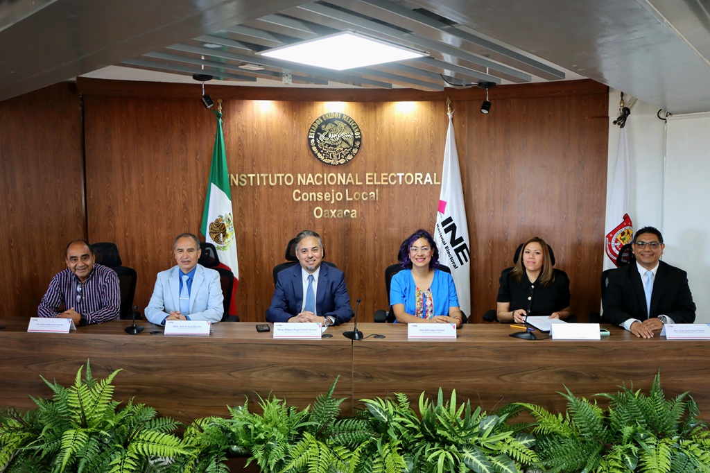 varias personas sentadas frente a una bandera de México y una del INE
