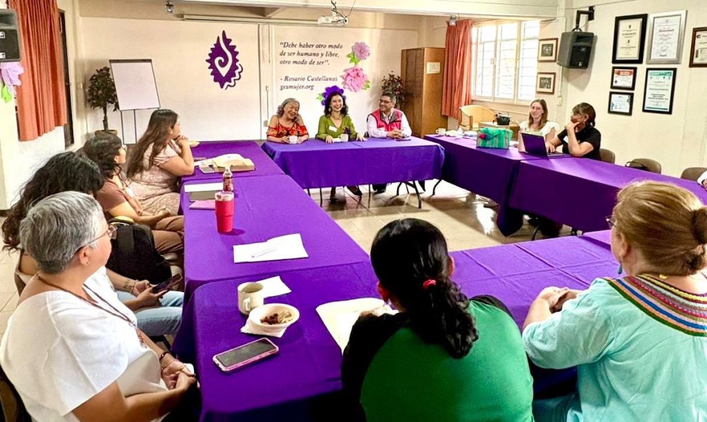 varias mujeres sentadas alrededor de una mesa cuadrada con mantel morado