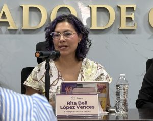 una mujer sentada de lentes hablando frente a un micrófono