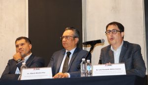 tres hombres sentados, uno habla mediante micrófono