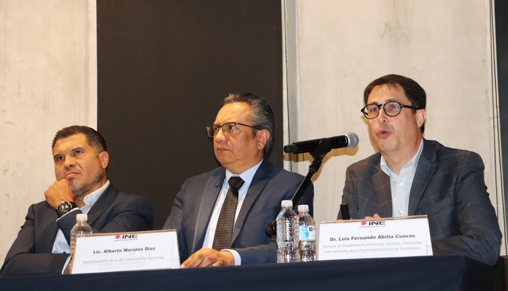 tres hombres sentados, uno habla mediante micrófono