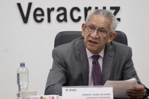 un hombre de pelo cano y lentes, sentado.