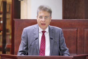 hombre de pie con saco gris y corbata guinda hablando