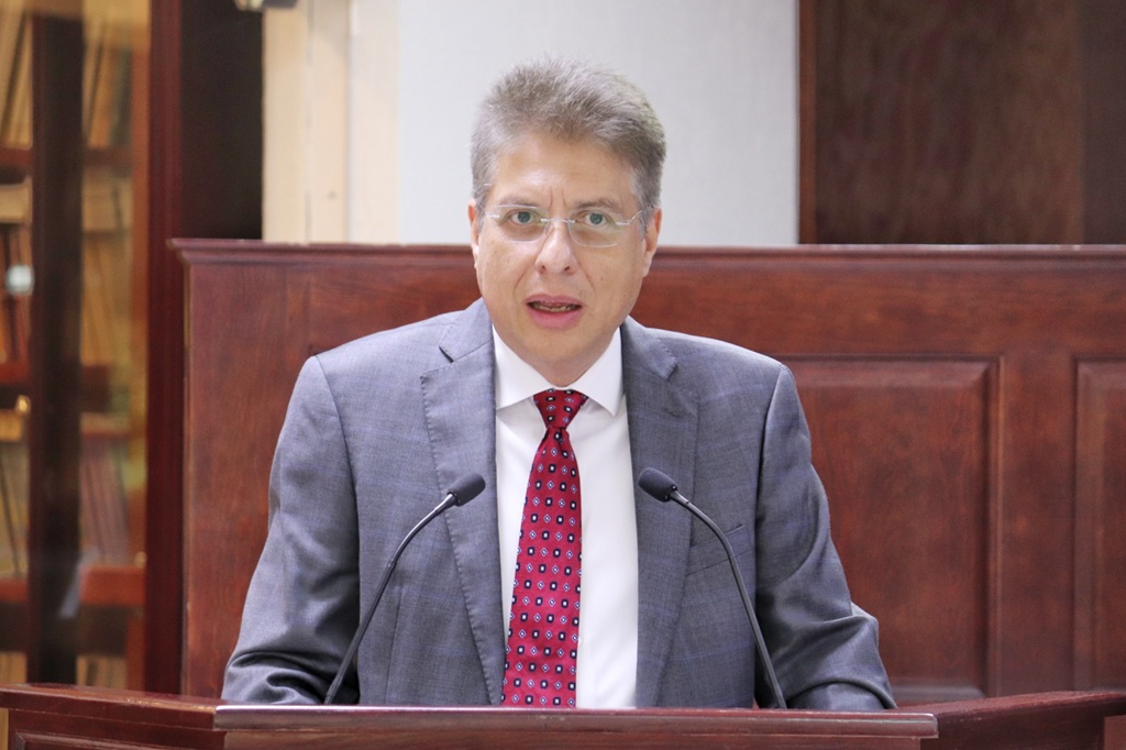 hombre de pie con saco gris y corbata guinda hablando