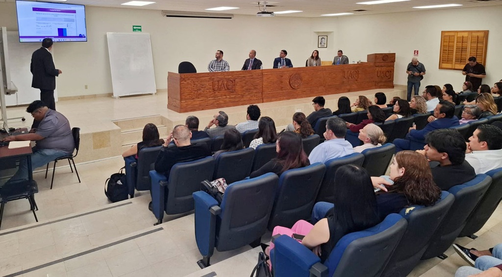 un hombre de pie hablando frente a personas sentadas en un auditorio