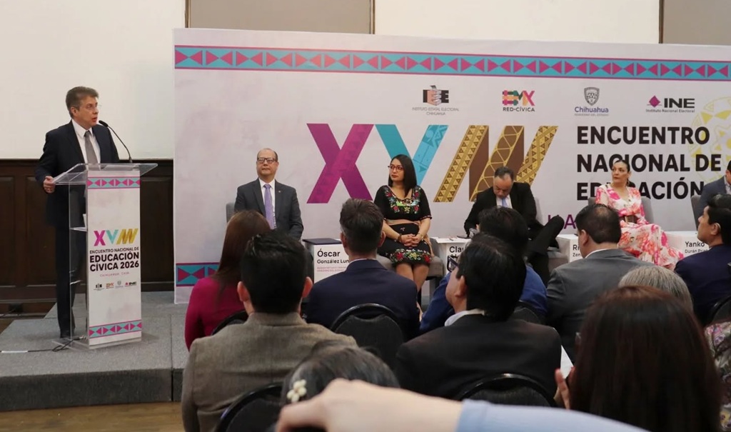 un hombre de pie detrás de un atril y varias personas sentadas a su lado