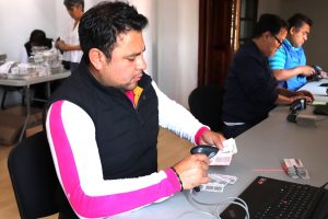 un hombre de chaleco negro sentado verificando códigos en las credenciales para votar sin validez