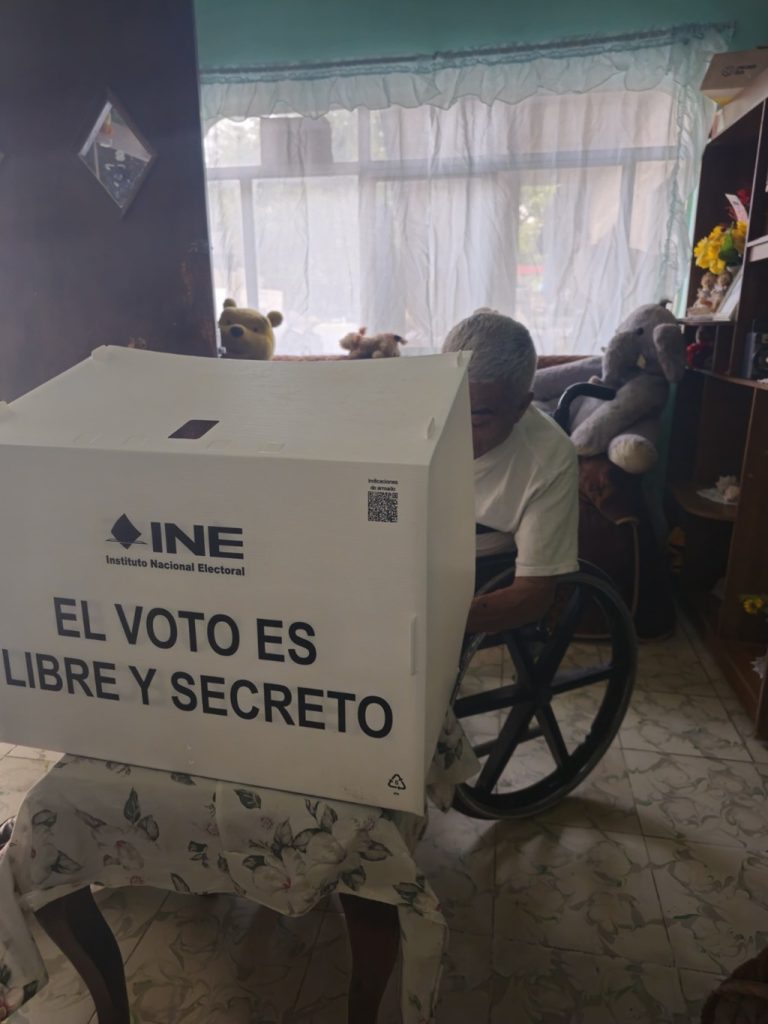 una persona adulta mayor en silla de ruedas votando desde su casa