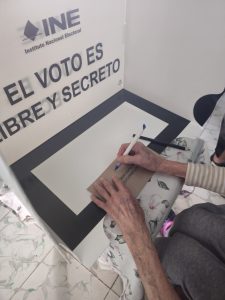 una persona adulta mayor ejerciendo el voto en una urna