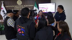 mujer rodeada de personas con cámaras y micrófonos