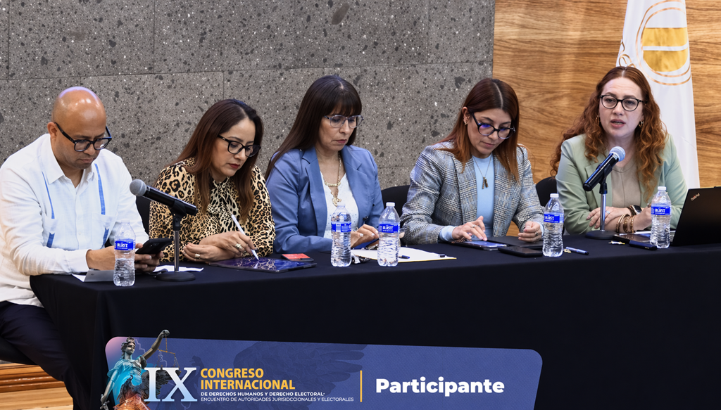 cuatro mujeres sentadas tres escriben y una habla a través de un micrófono