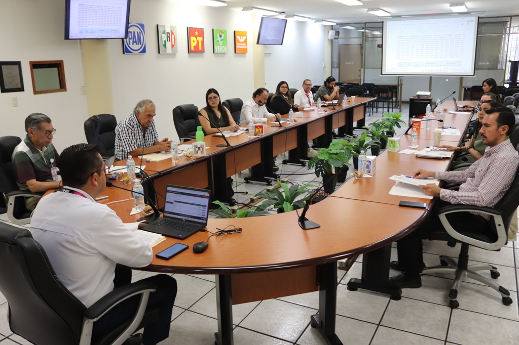 personas sentadas en una mesa ovalada viendo una pantalla