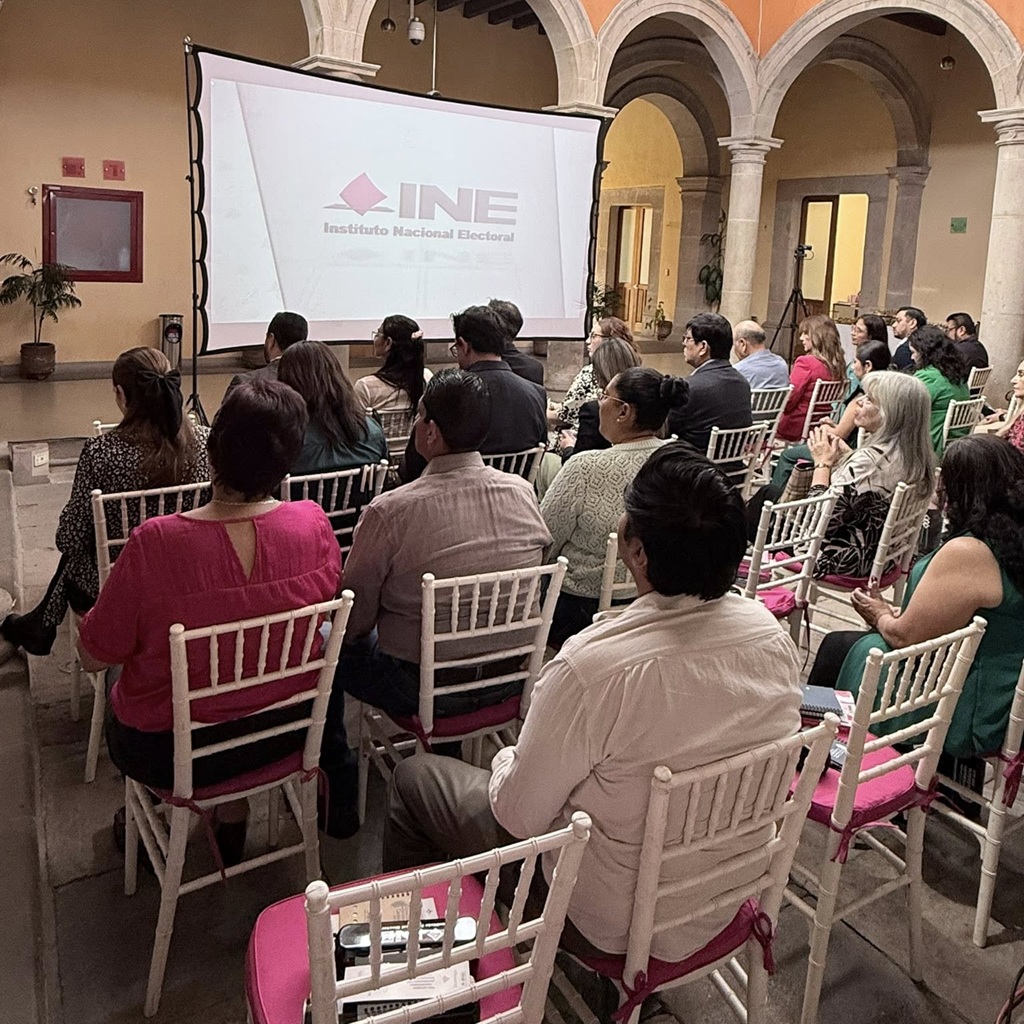 varias personas sentadas viendo una pantalla con las letras INE