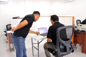 un hombre asesorando a otro que esta sentado frente a una computadora