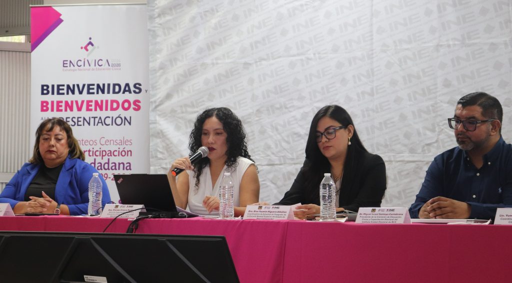 tres mujeres y un hombre sentadas detrás de una mesa con mantel rosa