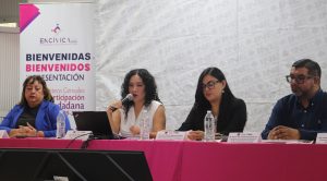 tres mujeres y un hombre sentadas detrás de una mesa con mantel rosa