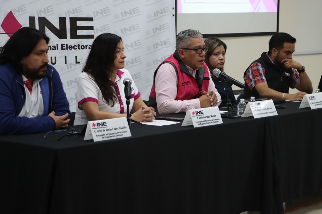 dos mujeres y tres hombres sentados frente a una mesa con micrófonos