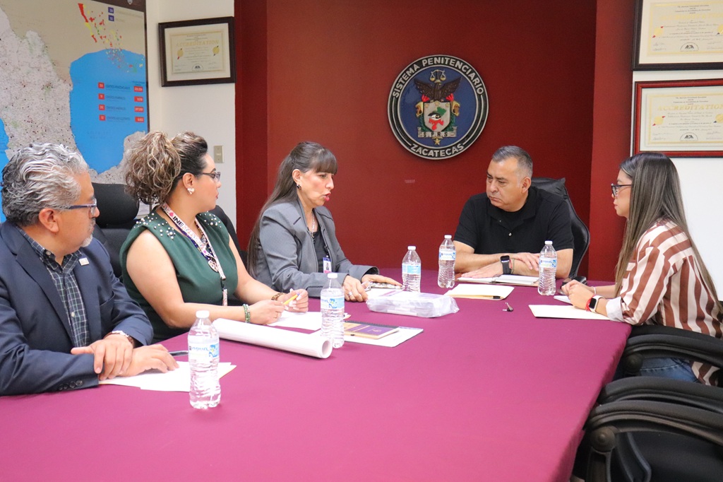tres mujeres y dos hombres sentados alrededor de una mesa conversando
