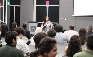 una mujer cabello largo, hablando frente a estudiantes