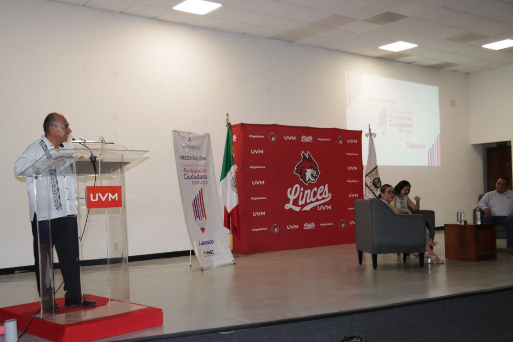 un hombre con guayabera de pie hablando frente a un atril