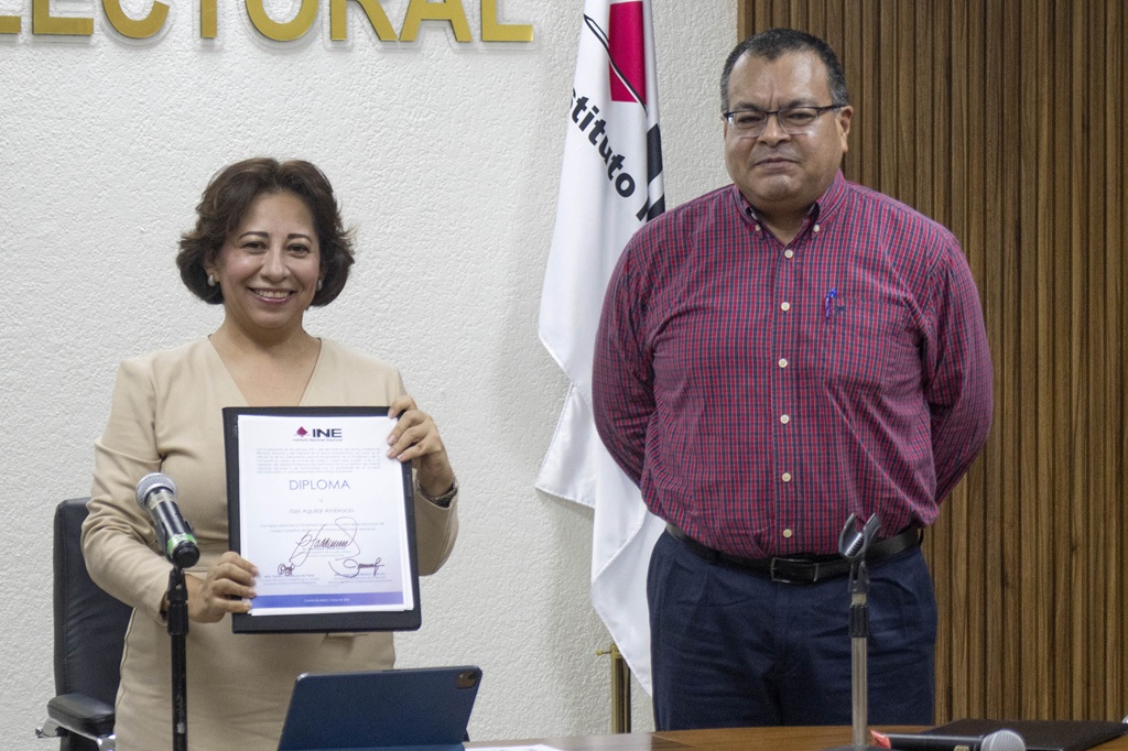 Una mujer de pie sosteniendo do un diploma, a su lado un hombre