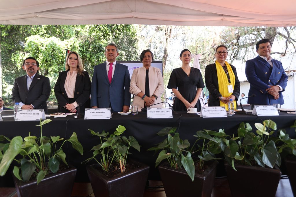 Personas Consejeras Electorales parados en el estrado frente al público asistente.