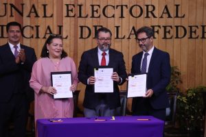 Personas participantes paradas en el estrado con el documento en la mano posado para la foto.