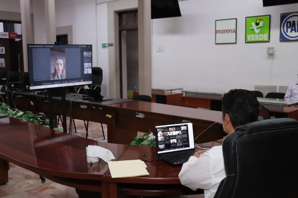 Participante sentado en el salón de Consejo frente a Pantalla con la imagen de la Consejera Carla Humphrey