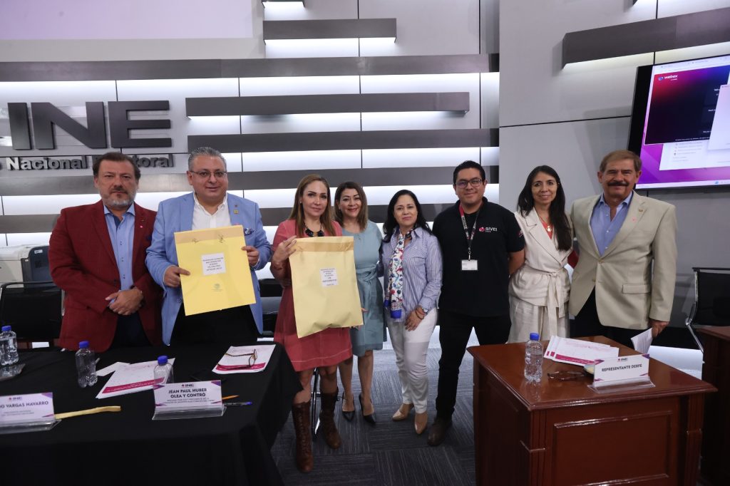 Personas participantes parada en el estrado posando para la foto mostrando sobres.
