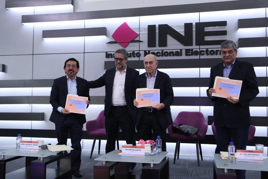 Personas participantes parados en el estrado del auditorio con su reconocimiento en las manos.