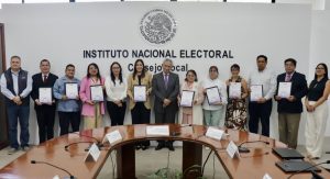 trece personas de pie, nueve sostienen diplomas