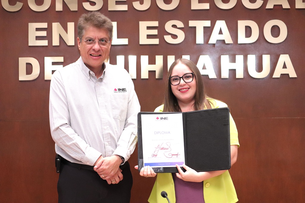 una mujer sosteniendo un diploma, a su lado un hombre de pie
