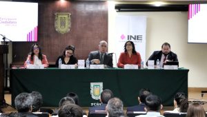 tres mujeres y dos hombres sentados frente a una mesa con micrófonos