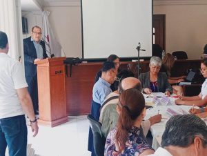 un hombre frente a un atril de madera hablando con personas sentadas