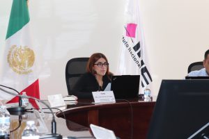 Una mujer cabello rojizo de lentes sentada frente a un micrófono