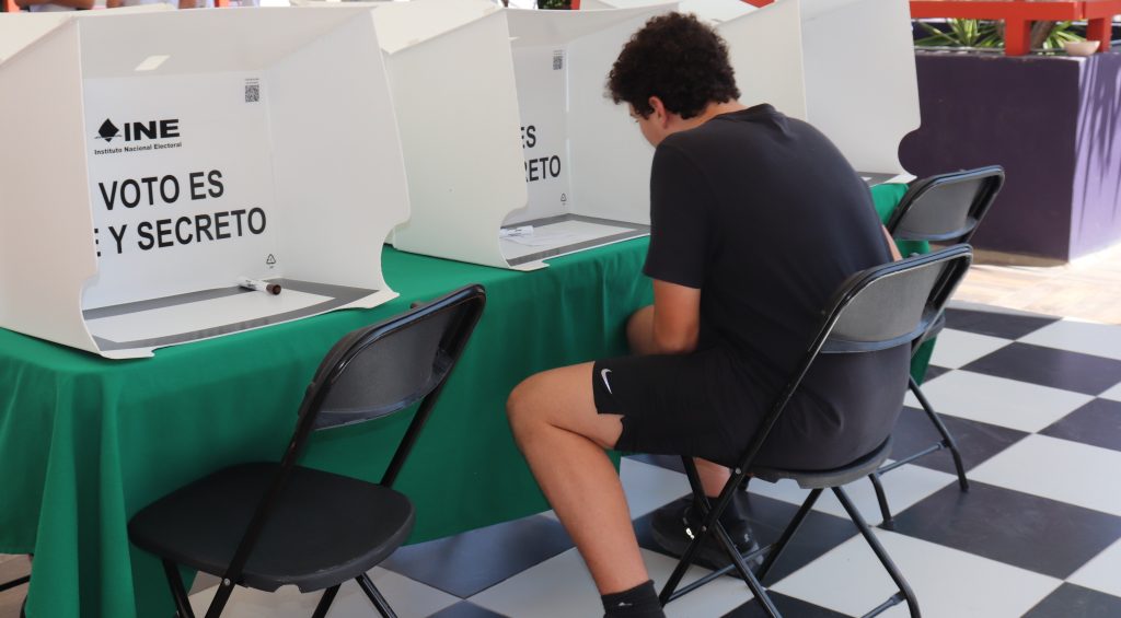 Un joven sentado frente a una urna electrónica de votación
