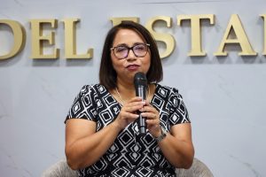 mujer cabello arriba de los hombros negro con lentes hablando con un micrófono en sus manos