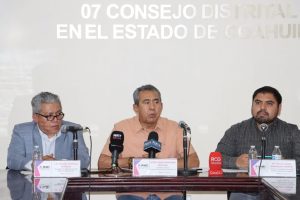 tres hombres sentados frente a varios micrófonos de medios